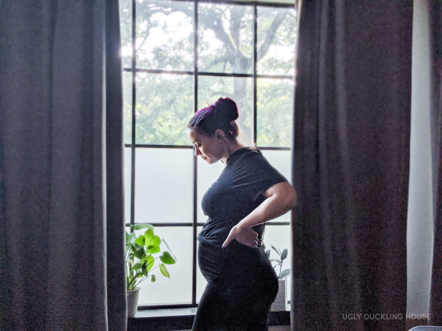 standing in the window with pregnancy bump and houseplants